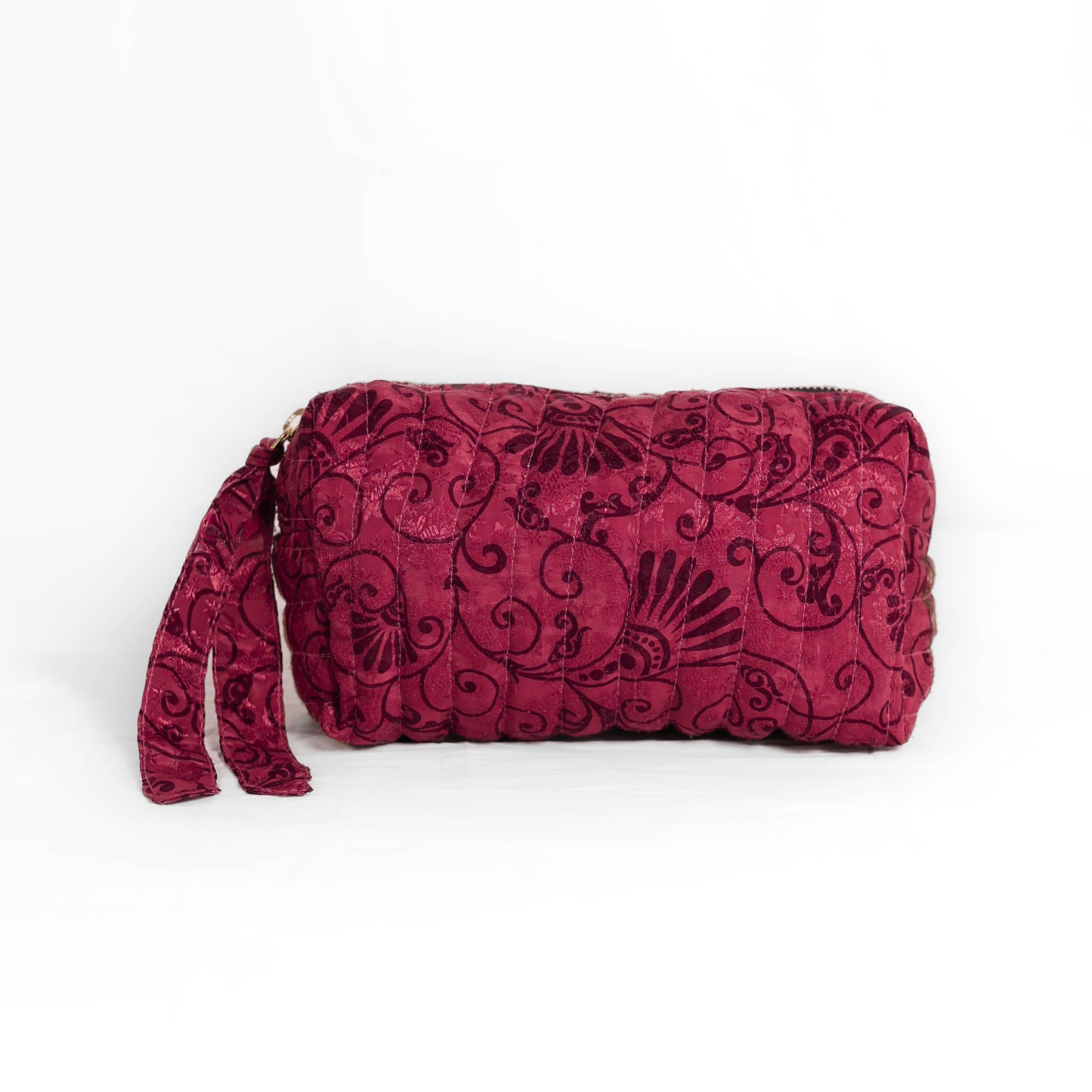 Quilted dumpling bag made from repurposed vintage sari fabric with stitched detailing and a structured rectangular shape. The bag features a zip closure and a fabric tie