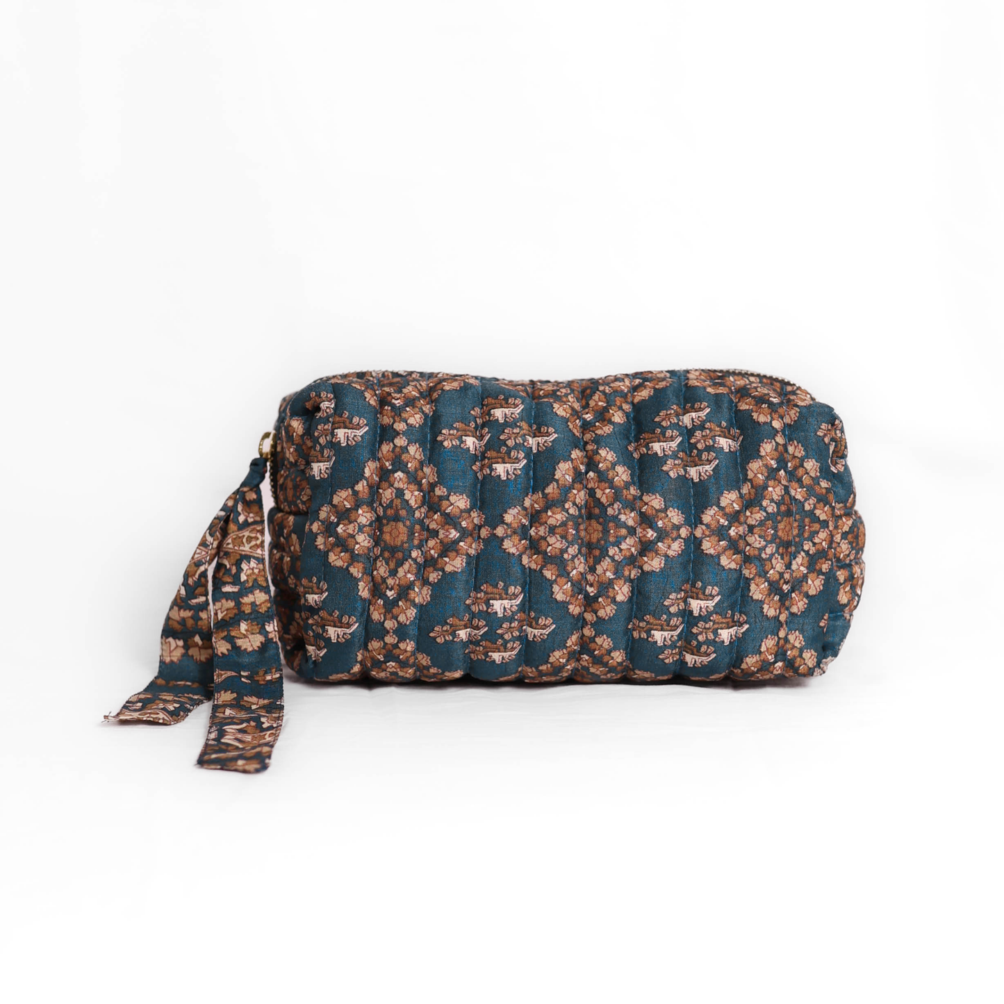 Quilted dumpling bag made from repurposed vintage sari fabric with stitched detailing and a structured rectangular shape. The bag features a zip closure and a fabric tie