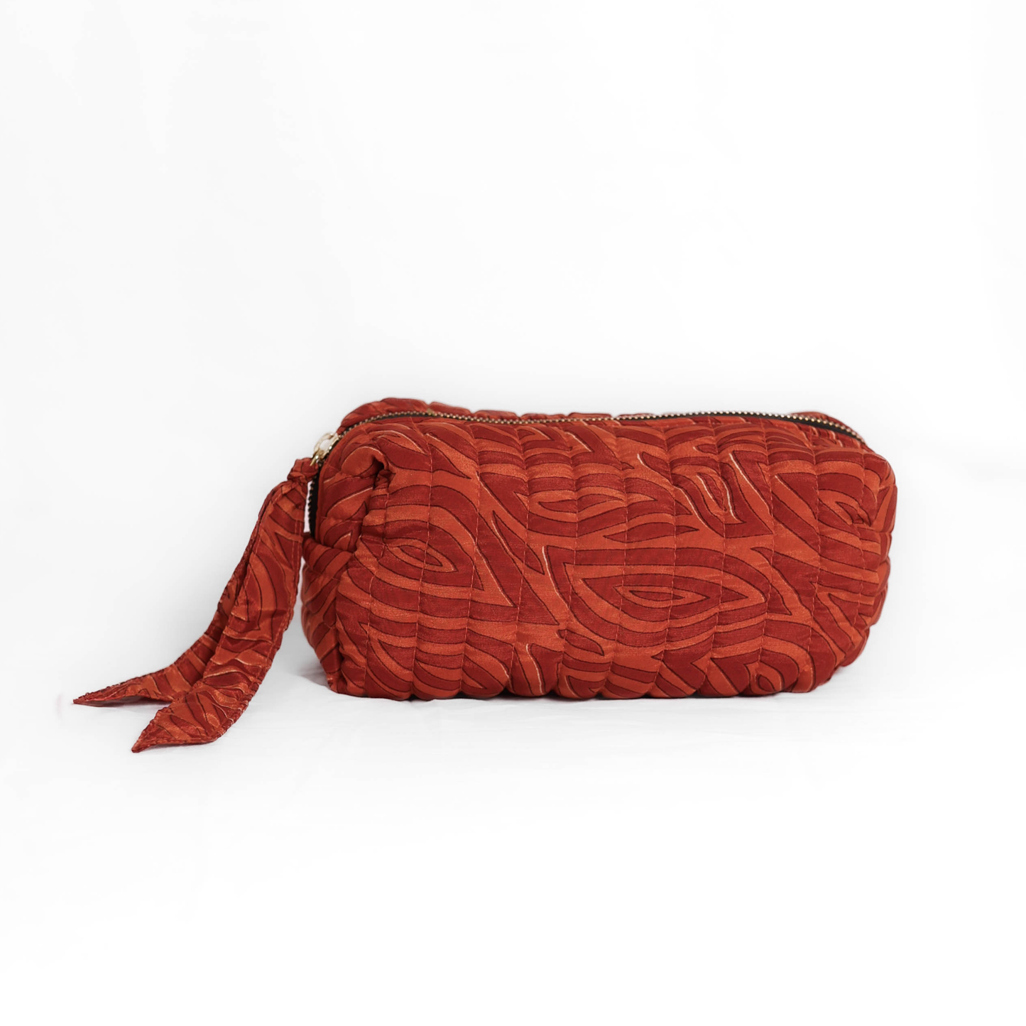 Quilted dumpling bag made from repurposed vintage sari fabric with stitched detailing and a structured rectangular shape. The bag features a zip closure and a fabric tie