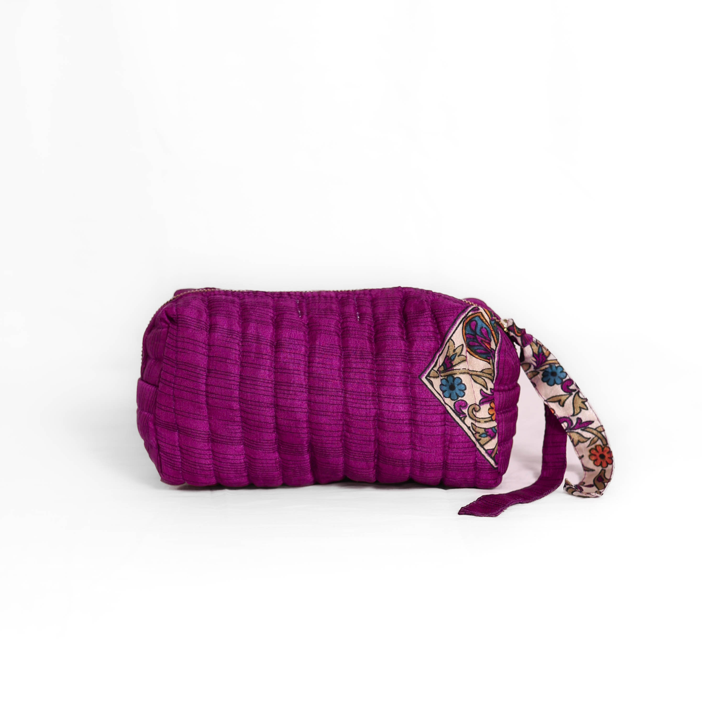 Quilted dumpling bag made from repurposed vintage sari fabric with stitched detailing and a structured rectangular shape. The bag features a zip closure and a fabric tie
