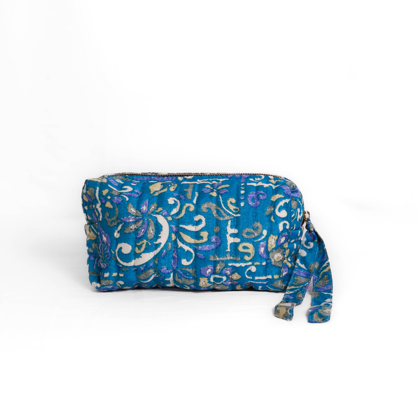 Quilted dumpling bag made from repurposed vintage sari fabric with stitched detailing and a structured rectangular shape. The bag features a zip closure and a fabric tie
