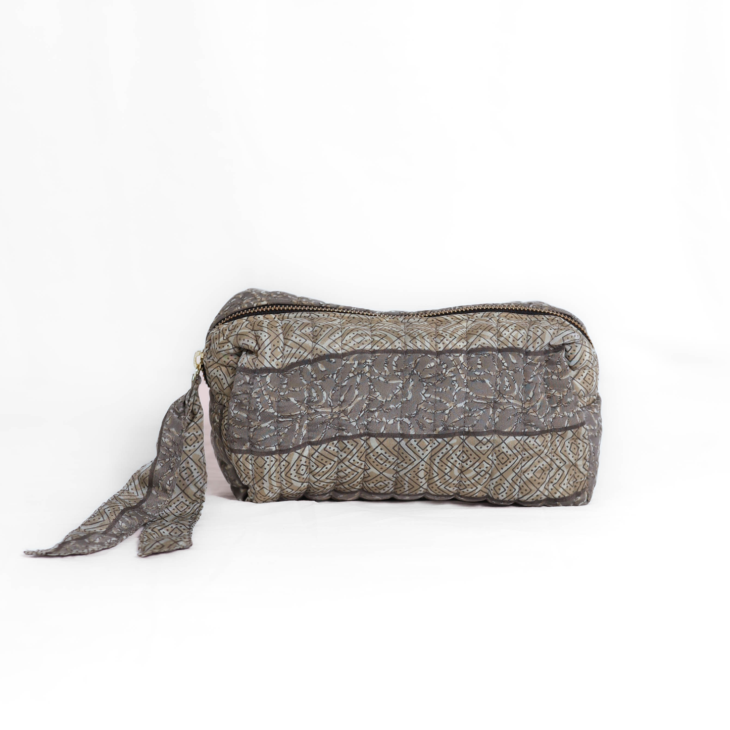 Quilted dumpling bag made from repurposed vintage sari fabric with stitched detailing and a structured rectangular shape. The bag features a zip closure and a fabric tie
