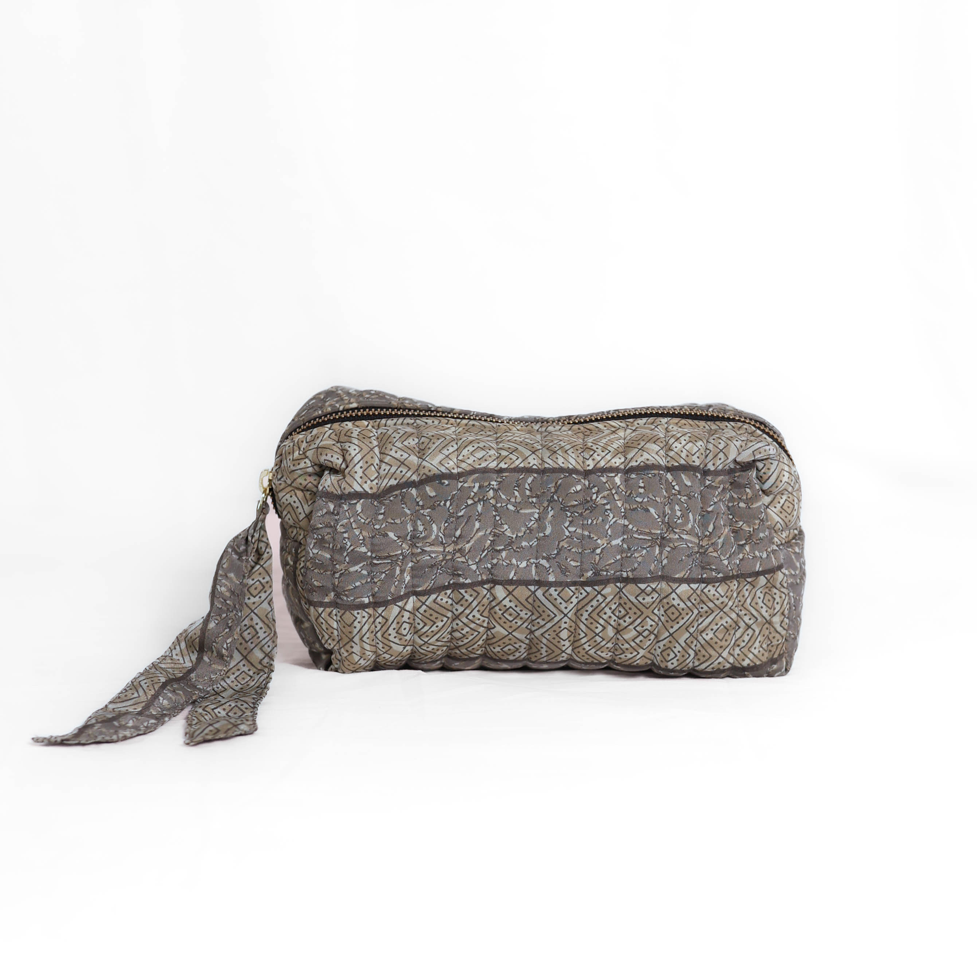 Quilted dumpling bag made from repurposed vintage sari fabric with stitched detailing and a structured rectangular shape. The bag features a zip closure and a fabric tie
