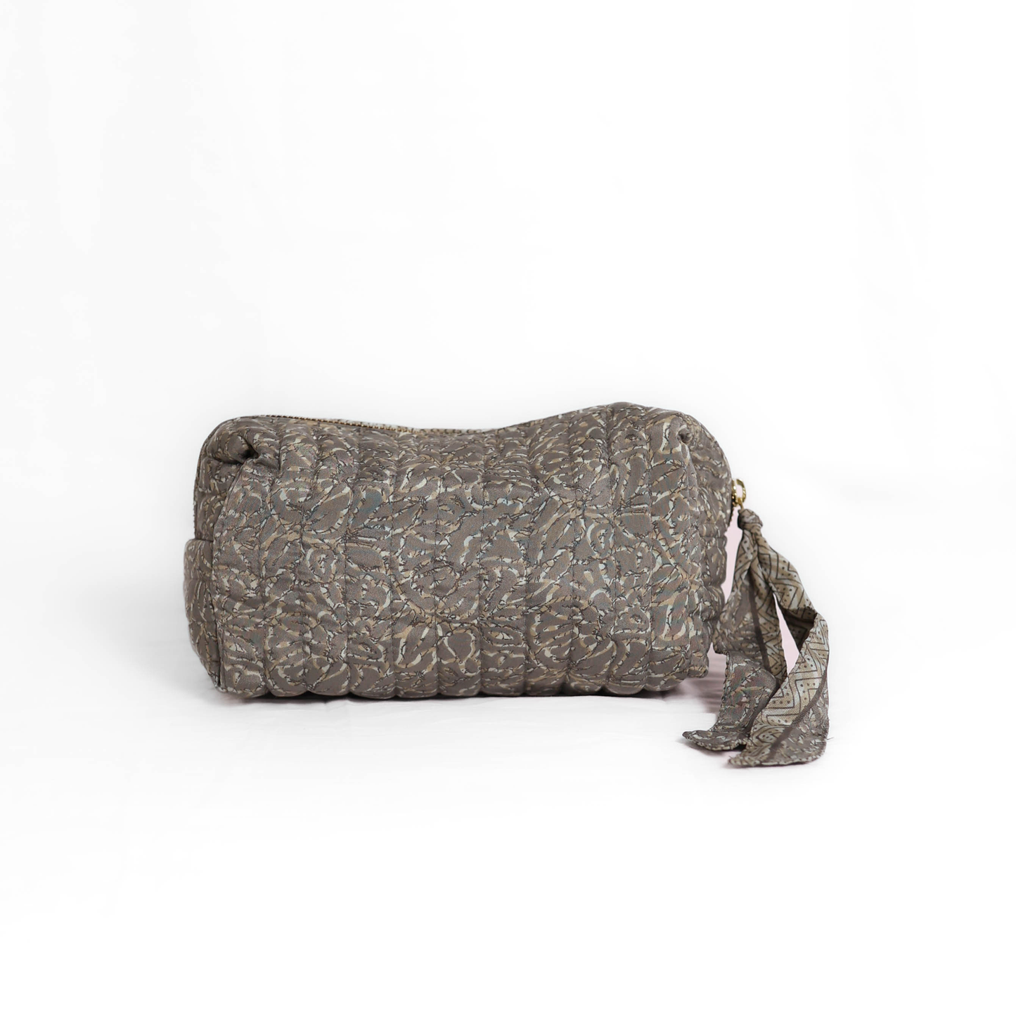 Quilted dumpling bag made from repurposed vintage sari fabric with stitched detailing and a structured rectangular shape. The bag features a zip closure and a fabric tie
