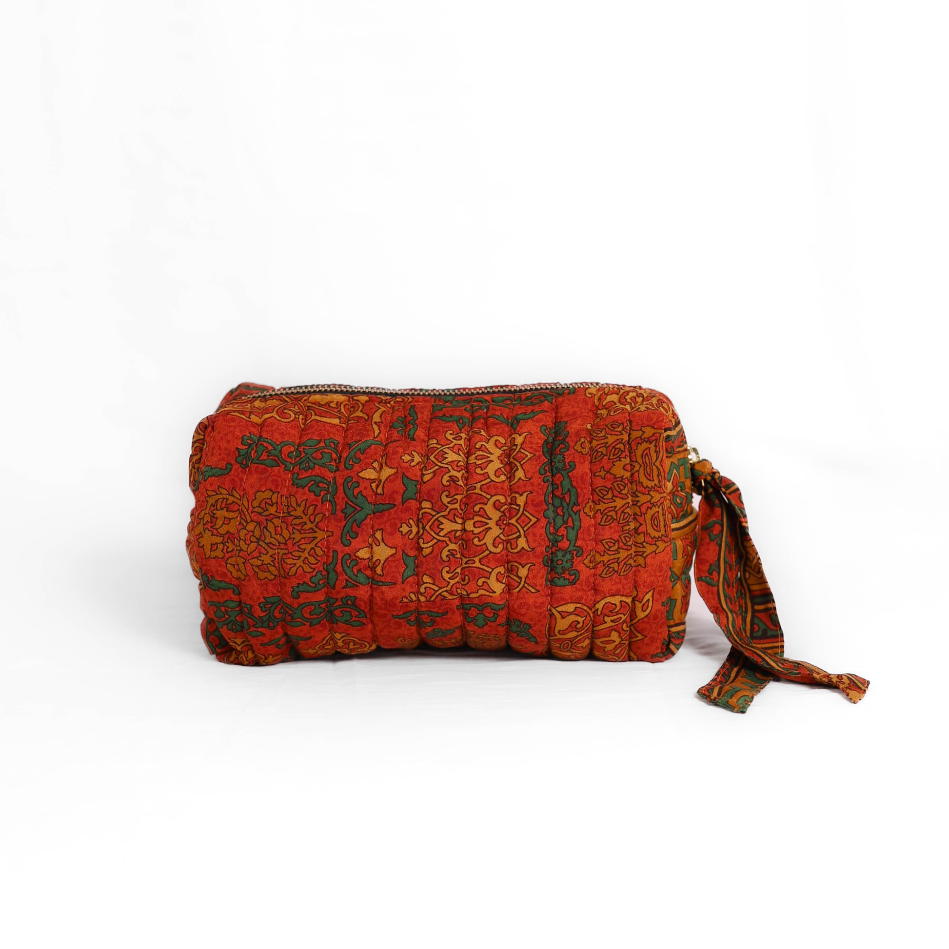 Quilted dumpling bag made from repurposed vintage sari fabric with stitched detailing and a structured rectangular shape. The bag features a zip closure and a fabric tie
