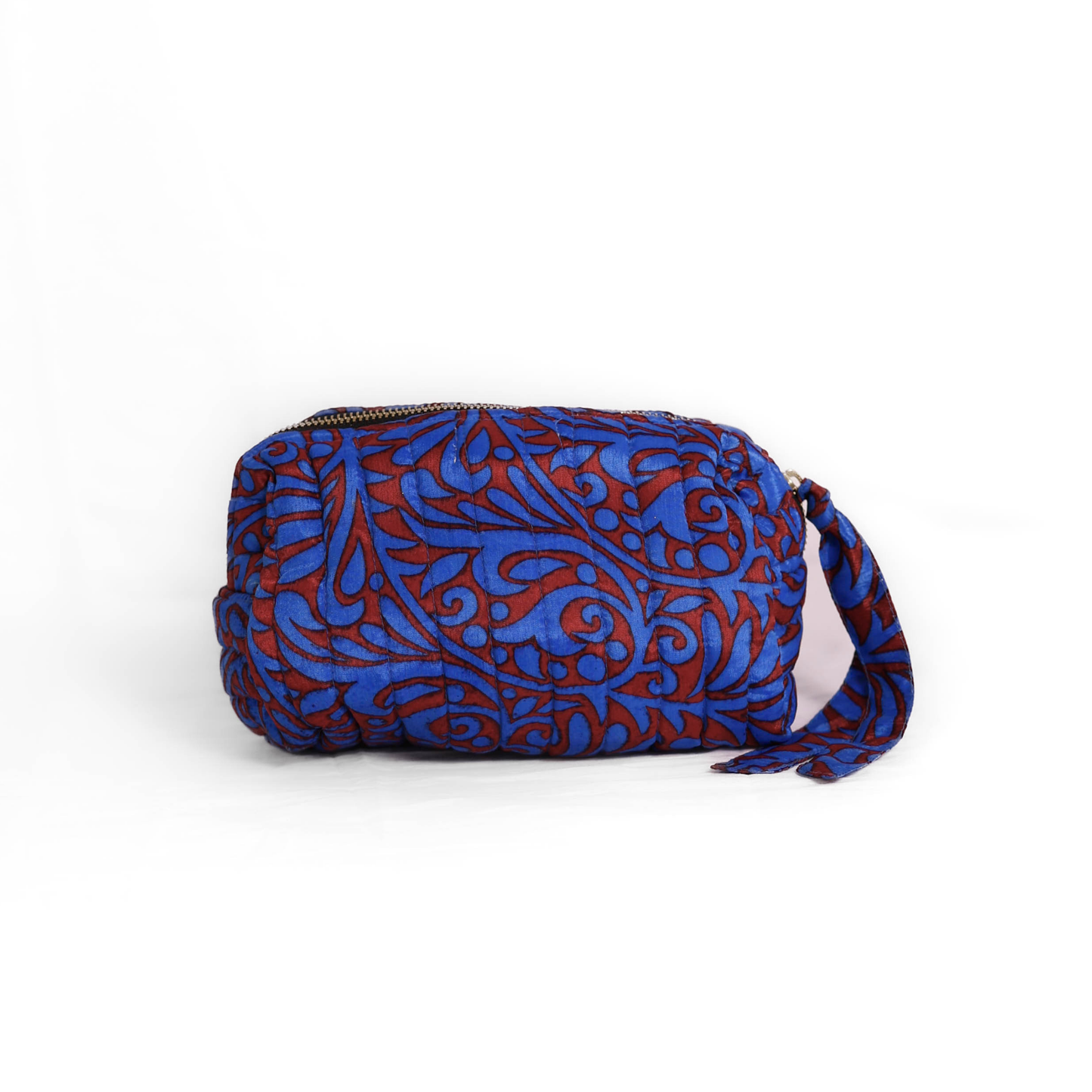Quilted dumpling bag made from repurposed vintage sari fabric with stitched detailing and a structured rectangular shape. The bag features a zip closure and a fabric tie