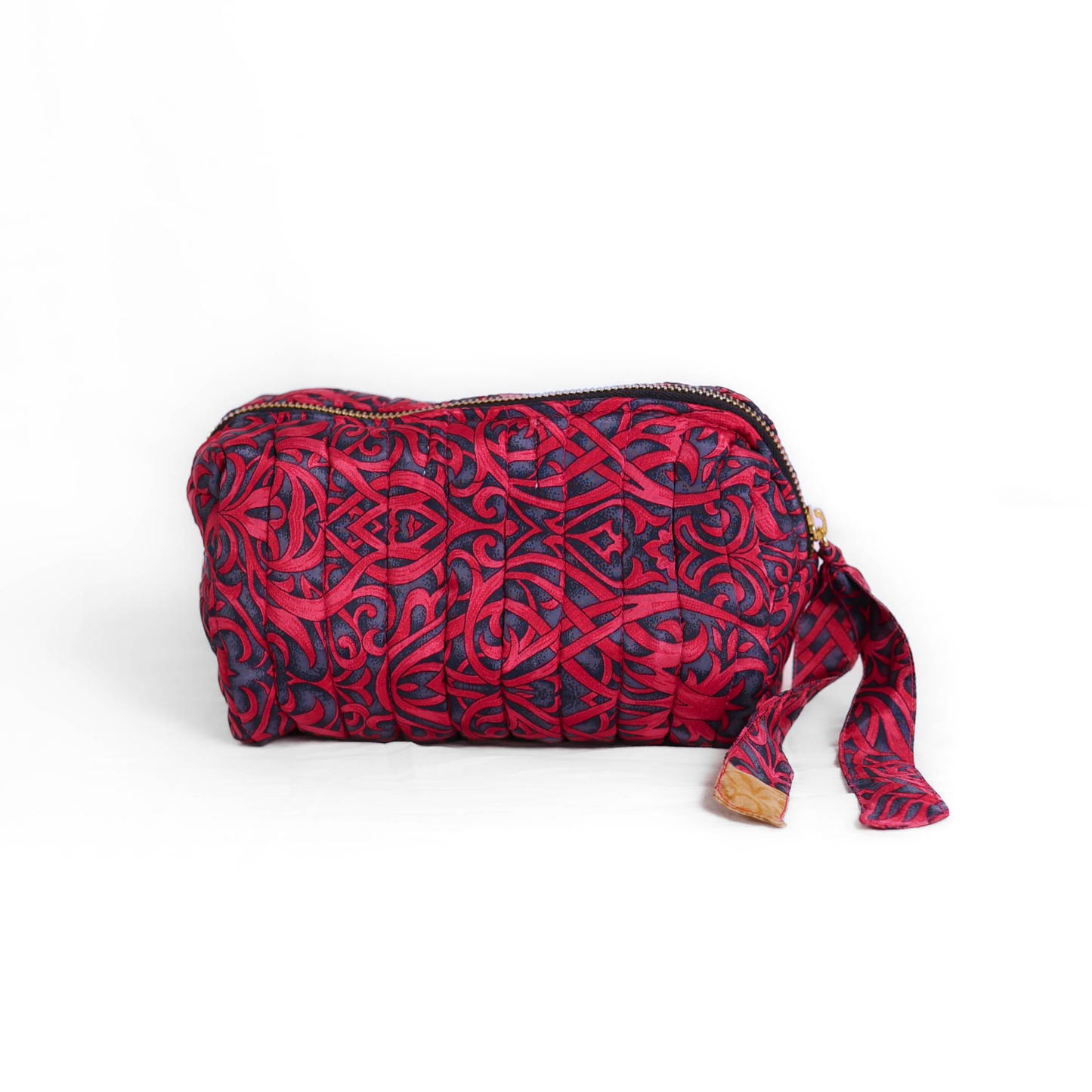Quilted dumpling bag made from repurposed vintage sari fabric with stitched detailing and a structured rectangular shape. The bag features a zip closure and a fabric tie