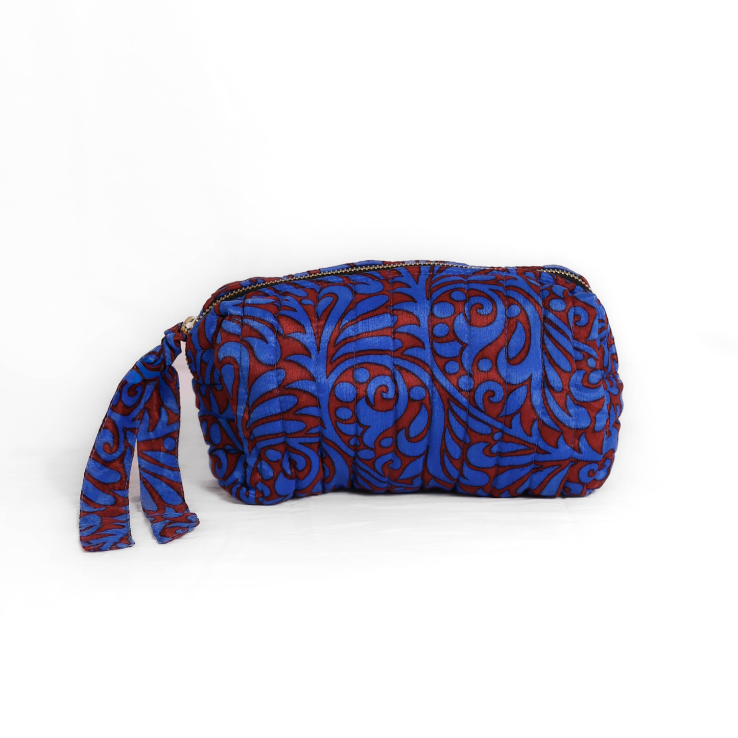 Quilted dumpling bag made from repurposed vintage sari fabric with stitched detailing and a structured rectangular shape. The bag features a zip closure and a fabric tie
