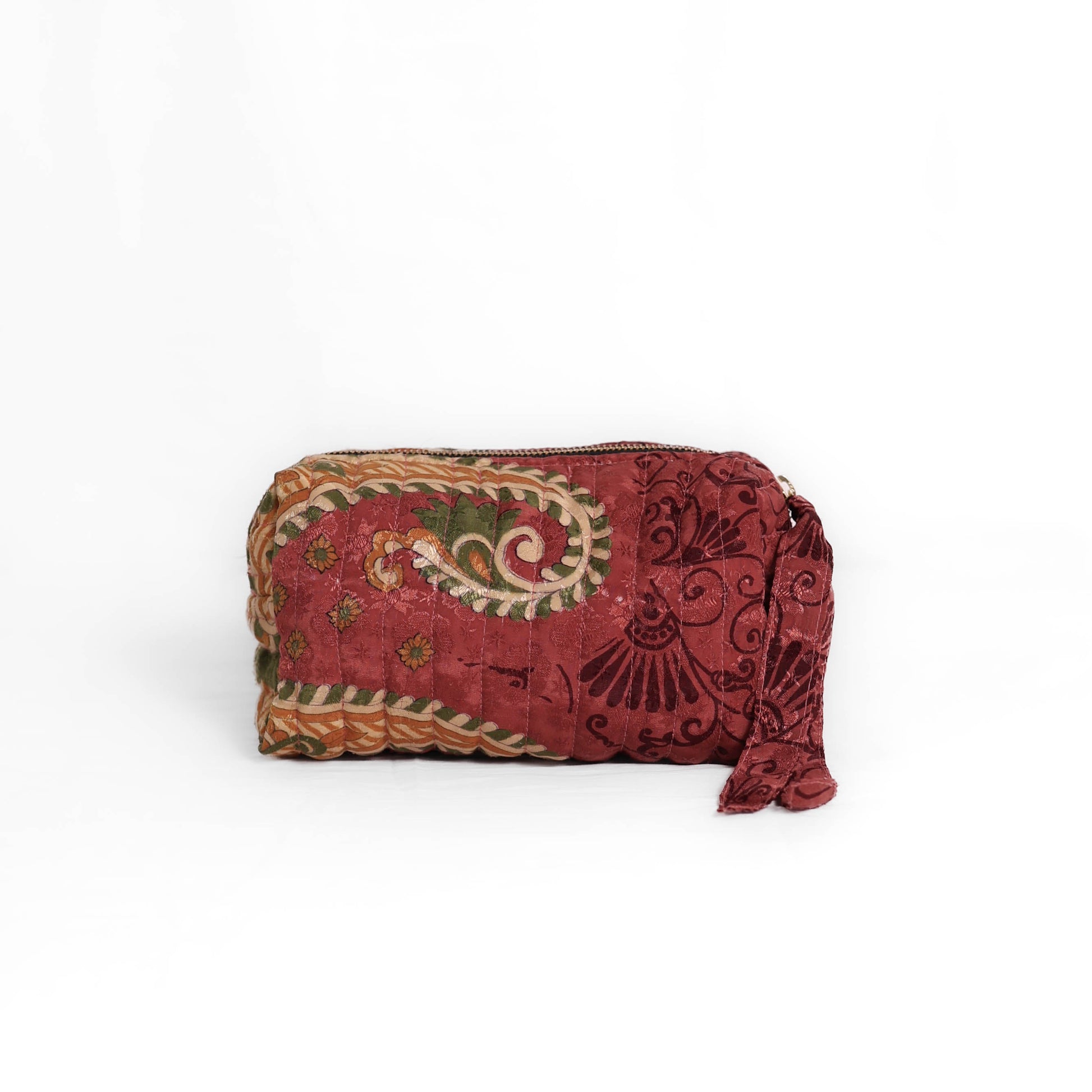 Quilted dumpling bag made from repurposed vintage sari fabric with stitched detailing and a structured rectangular shape. The bag features a zip closure and a fabric tie
