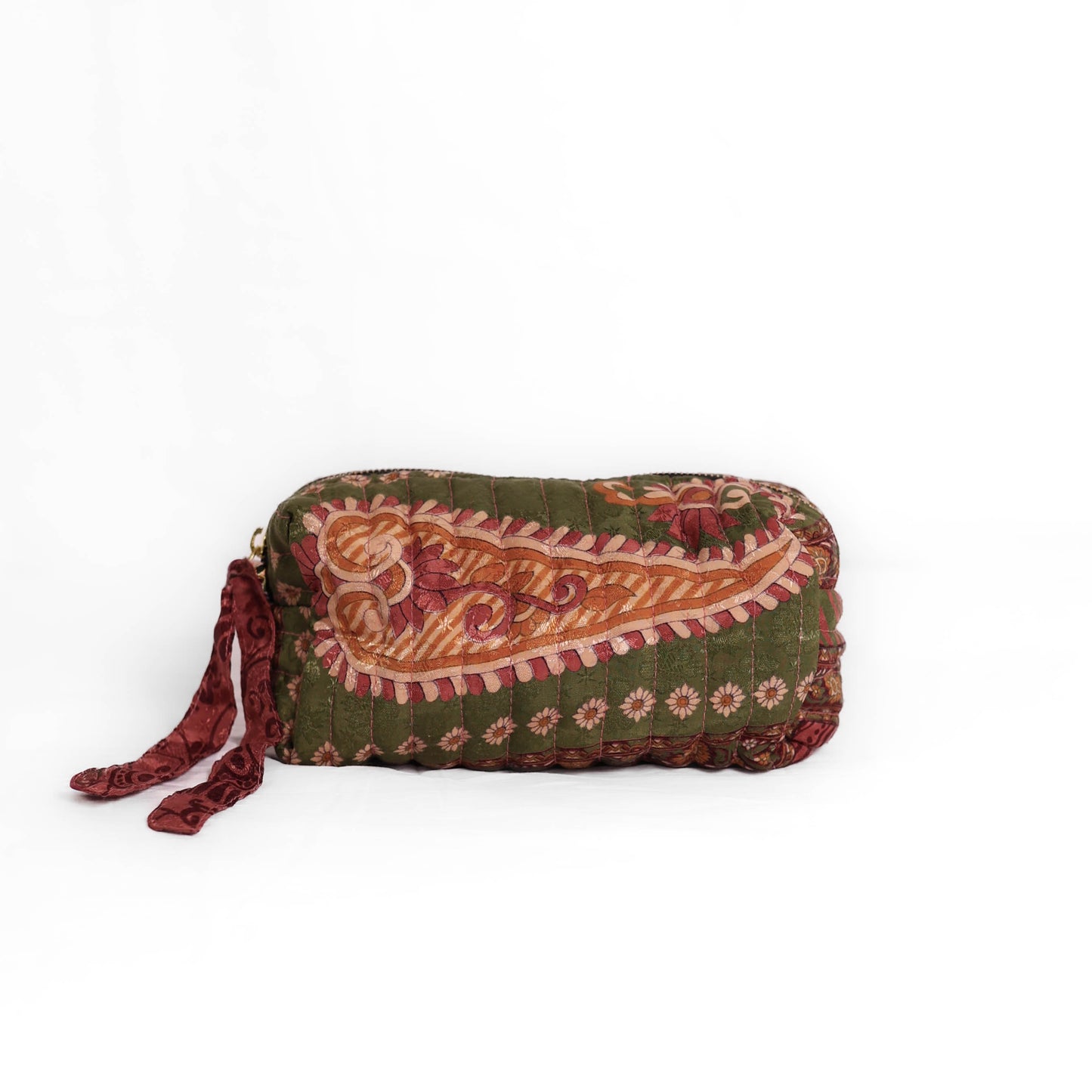 Quilted dumpling bag made from repurposed vintage sari fabric with stitched detailing and a structured rectangular shape. The bag features a zip closure and a fabric tie
