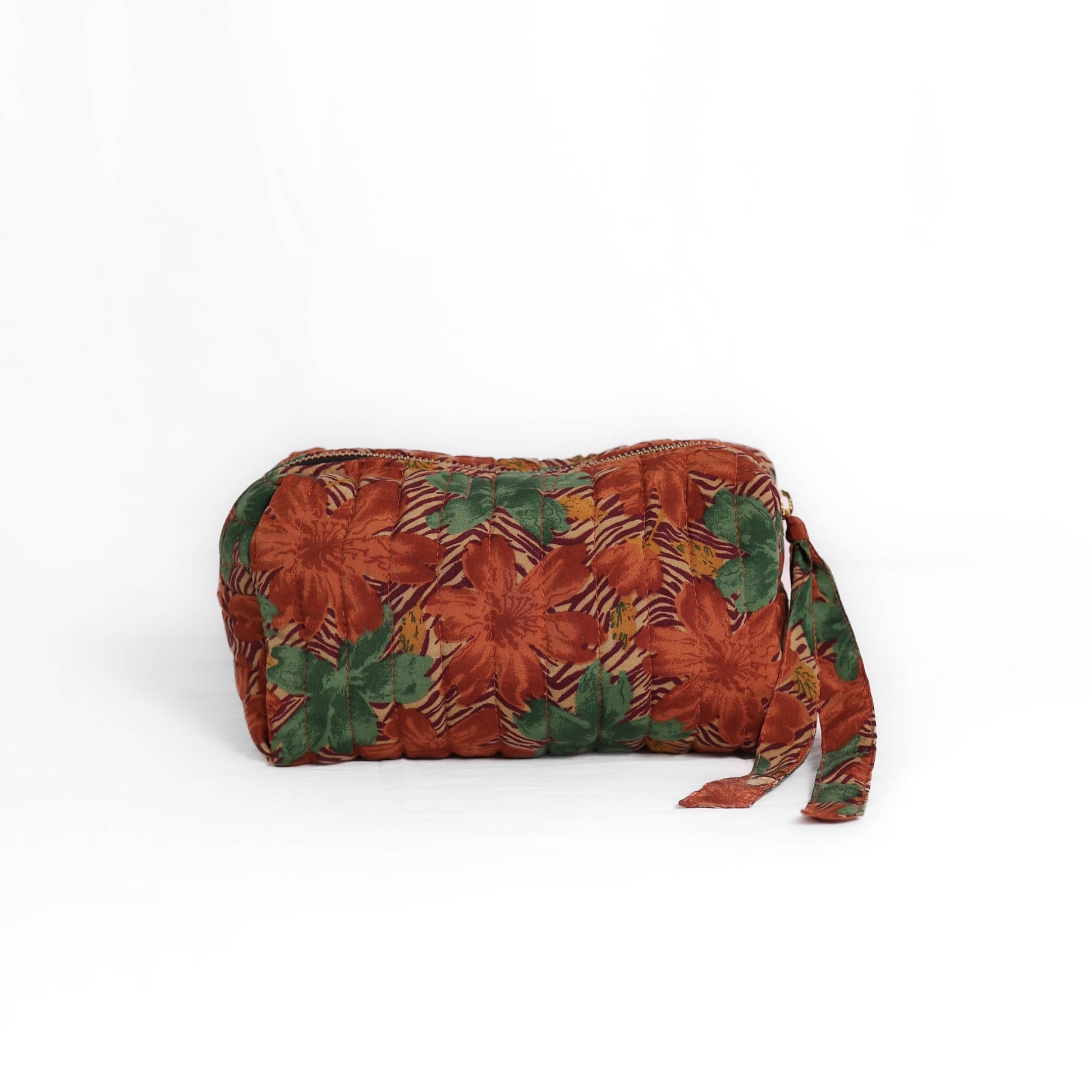 Quilted dumpling bag made from repurposed vintage sari fabric with stitched detailing and a structured rectangular shape. The bag features a zip closure and a fabric tie
