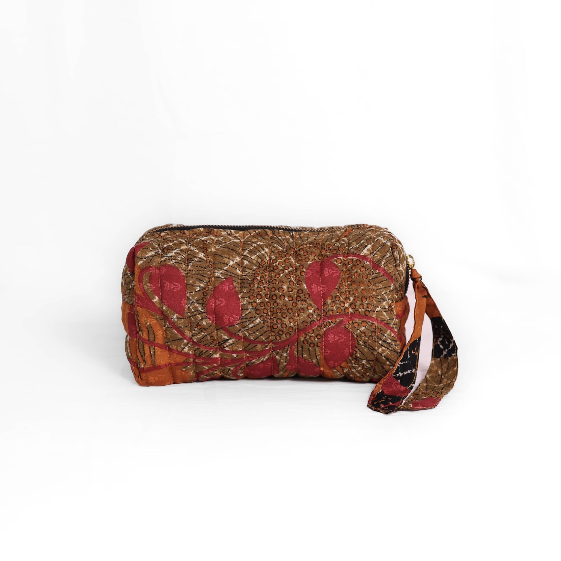 Quilted dumpling bag made from repurposed vintage sari fabric with stitched detailing and a structured rectangular shape. The bag features a zip closure and a fabric tie
