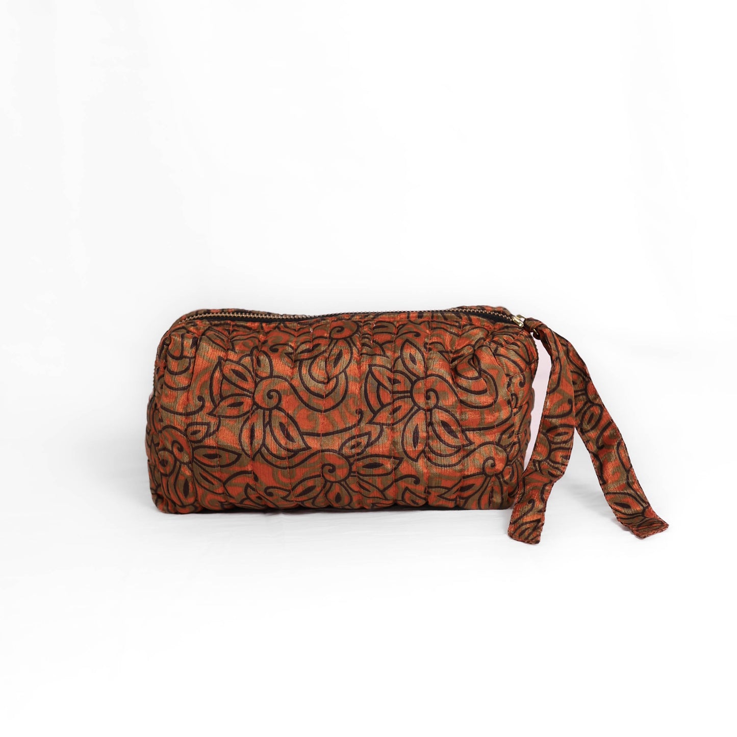 Quilted dumpling bag made from repurposed vintage sari fabric with stitched detailing and a structured rectangular shape. The bag features a zip closure and a fabric tie
